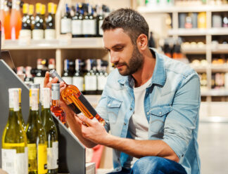 This is perfect wine! Handsome young man holding bottle of wine while standing in a wine store This is perfect wine! Handsome young man holding bottle of wine while standing in a wine store